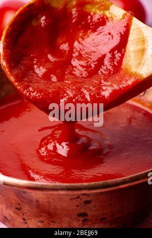 Schöpfkelle im Vordergrund mit frischer, hausgemachter Tomatensoße Stockfoto