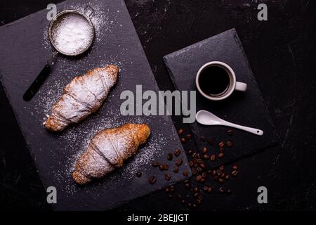 Draufsicht, Tasse schwarzen Kaffee und Croissants mit verhülltem Zucker auf dunklem Hintergrund Stockfoto