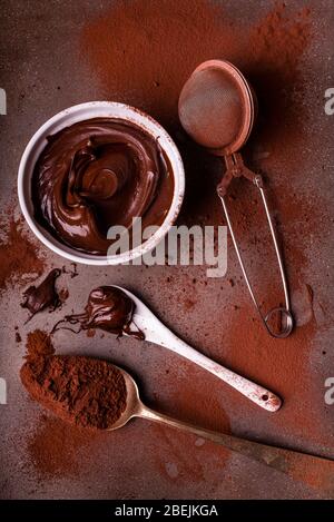 Draufsicht, Keramikschale mit dunkler Schokoladencreme, Löffel mit Schokolade bedeckt und bestreuen von Kakao auf dem Hintergrund Stockfoto