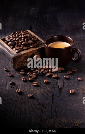 Auf dem rohen und dunklen Holztisch eine Tasse heißen Kaffee und eine Schublade einer alten Mühle mit gerösteten Kaffeebohnen. Stillleben Stockfoto