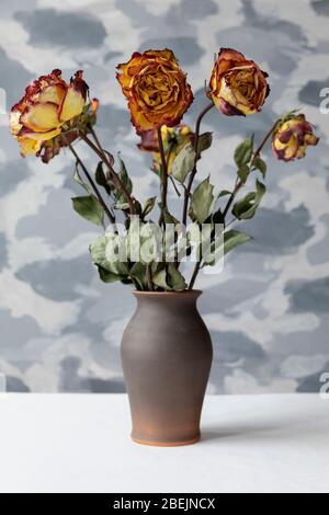 Bouquet von verwelkten mehrfarbigen Rosen in brauner Keramikvase. Grauer Wandhintergrund. Stockfoto