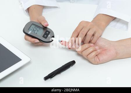 Diabetes prüfen. Patienten mit Diabetes lassen Arzt einen Tropfen Blut auf einen Teststreifen in ein Messgerät für die Kontrolle Blutzucker (Glukose) Ergebnisse. Heilen Stockfoto