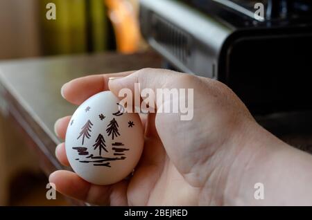 Auf ein Hühnereier zeichnen. Die Hand hält ein rohes Ei mit einem Landschaftsbild auf der Schale. Nahaufnahme. Selektiver Fokus. Stockfoto