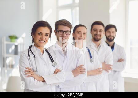 Eine Gruppe von selbstbewussten Praktizierenden Ärzten in weißen Mänteln lächelt vor dem Hintergrund der Klinik. Stockfoto