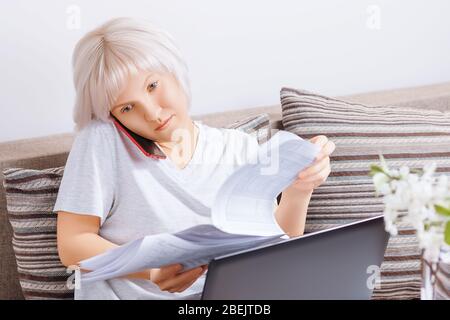 Nette beschäftigt junge Frau schaut auf Finanzdokumente und Berichte während des Gesprächs am Telefon aus dem Home Office. Telearbeit, freiberuflich, selbsttätig Stockfoto