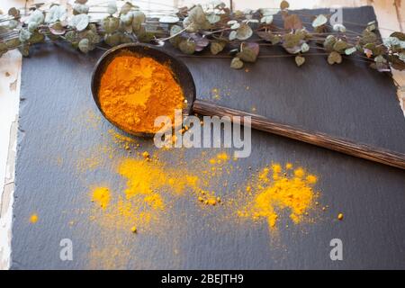 Kurkuma auf einem Holzlöffel, der auf schwarzen Schiefer verschüttet wird Stockfoto