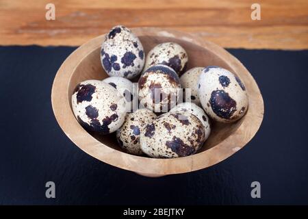 Ein Studiofoto von Wachteln Eier in einer Holzschüssel auf einem Stück schwarzen Schiefer Stockfoto