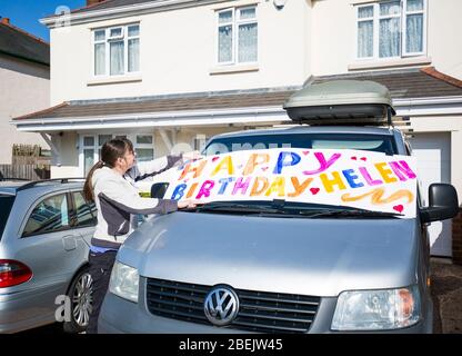 Kidderminster, Großbritannien. April 2020. Mit Großbritannien in Lockdown und viele Menschen verbringen Geburtstage allein ohne Freunde oder Familie, ist es an Nachbarn, um die Rettung kommen! Obwohl sie sich selbst isolieren muss, kommt diese Dame mit einer provisorischen Art und Weise, einem Nachbarn, der direkt auf der anderen Straßenseite wohnt, besondere Geburtstagswünsche zu senden. Mit einem riesigen selbstgemachten Banner aus Karte und Farben (gefunden auf der Rückseite der Garage!) Sie zeigt es auf der Windschutzscheibe ihres Fahrzeugs, das auf dem Laufwerk steht. Nach sozialen Distanzierungsregeln gibt es keinen Kontakt, aber die Botschaft ist klar! Kredit: Lee Hudson/Alamy Live News Stockfoto