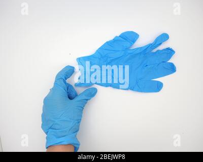 Hand mit EINEM blauen Einweghandschuh (PSA), der nach draußen greift und eine Schutzbrille in die Hand nimmt, London, Großbritannien Stockfoto