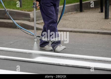 Details mit einem Straßenarbeiter, der einen Straßenüberweg auf einer Straße in der Stadt malt. Stockfoto