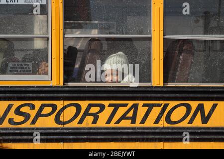 Kleines Mädchen mit weißer Mütze, das durch ein schmutziges Schulbusfenster in Lower East Side, Manhattan, New York City, USA, die Kamera anschaut Stockfoto