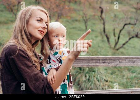 Mama hält Toddlers Tochter in den Armen und zeigt ihr etwas mit dem Finger. Stockfoto