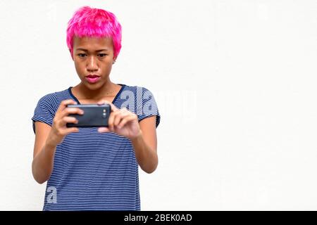 Junge rebellische asiatische Frau mit rosa Haar, die mit Telefon fotografieren Stockfoto