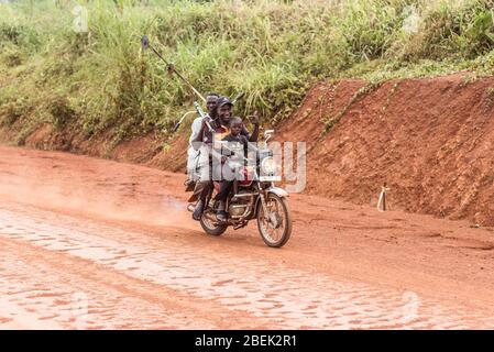 Fort Portal / Uganda - 30. September 2016: Drei Personen reisen mit altem Motorrad und tragen Werkzeuge auf einer Feldbahn in der ugandischen Landschaft Stockfoto