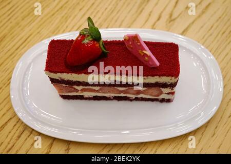 Auf dem Tisch eine Scheibe roter Samtkuchen. Serviert mit Rubinschokolade und Erdbeeren. Eine Scheibe Kuchen aus nächster Nähe Stockfoto