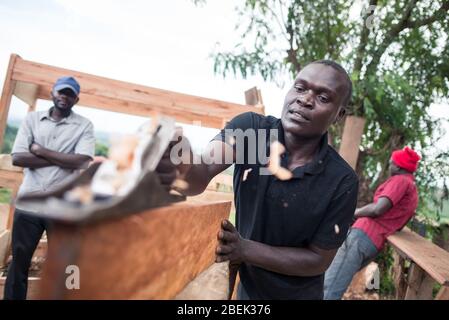 Fort Portal / Uganda - 30. September 2016: Zimmermann, der ein Holzblatt mit einem Werkzeug und Sägemehl in der Luft abfeilt Stockfoto