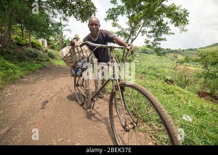 Fort Portal / Uganda - 30. September 2016: Ultra-Weitwinkel-Porträt eines Mannes, der sein Fahrrad auf einer Feldstraße in der ugandischen Landschaft zieht Stockfoto