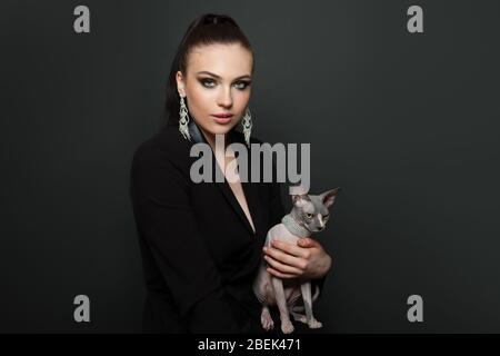 Attraktive Frau in Diamant-Ohrringe mit sphynx Katze auf schwarzem Hintergrund, Mode-Porträt Stockfoto