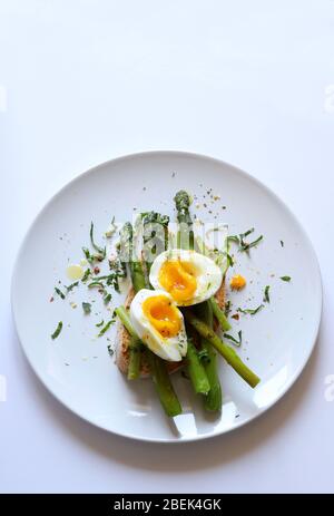 Frühstück Food Konzept.Tasty Toast mit Spargel, pochiertes Ei und Gewürz auf Teller auf weißem Hintergrund serviert. Draufsicht, Kopierbereich. Gesunde Ernährung. Stockfoto