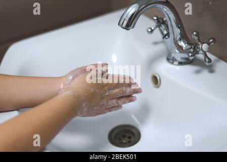 Waschen der Kinderhände mit der Seife unter dem Kran mit dem Wasser. Stockfoto