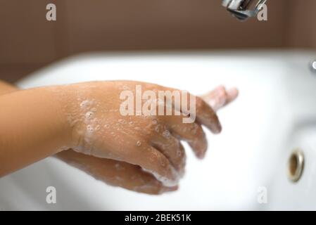 Waschen der Kinderhände mit der Seife unter dem Kran mit dem Wasser. Stockfoto