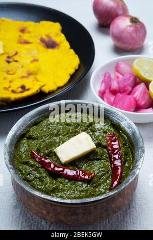 Sarso ka saag und makki KI roti auf einem Tisch mit eingelegten Zwiebeln gehalten. Stockfoto