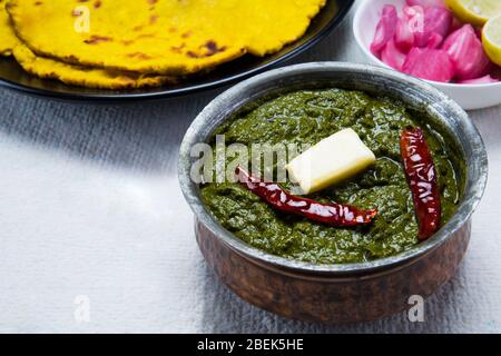 Sarso ka saag und makki KI roti auf einem Tisch mit eingelegten Zwiebeln gehalten. Stockfoto