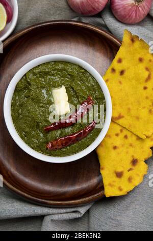 Köstliche Schale Sarso ka saag mit Makki KI Roti auf einem Holzteller gehalten. Stockfoto