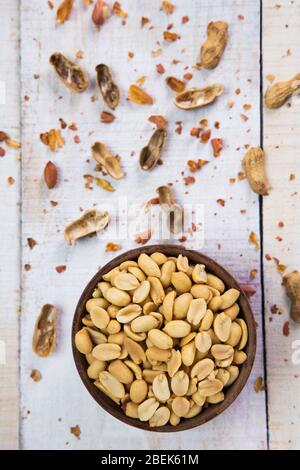 Einfache Erdnüsse in einer Holzschale zusammen mit rissigen Muscheln aufbewahrt. Stockfoto