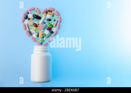 Glas von verschiedenen Tabletten und Pillen in Form von Herz auf sie. Mehrfarbige Pillen in Form von Herz auf. Konzept der Behandlung und des Gesundheitswesens Stockfoto