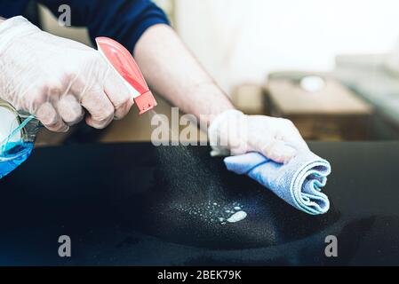 Nahaufnahme der Person, die Einweghandschuhe trägt und Desinfektionsmittel zur Reinigung der Tischoberfläche während der Coronavirus Covid-19-Pandemie verwendet Stockfoto