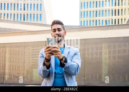 Porträt eines schönen jungen Mannes lächelnd, wenn er sein Handy benutzt Stockfoto