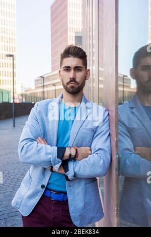 Junger bärtiger Mann mit verschränkten Armen, Modelein, im urbanen Hintergrund in lässiger Kleidung Stockfoto
