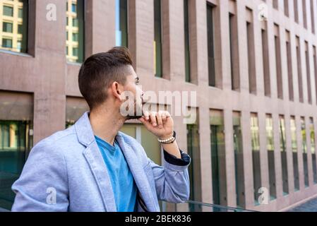 Bärtiger junger Mann, der sich mit der Hand auf dem Kinn auf einen Zaun lehnt und dabei wegschaut Stockfoto
