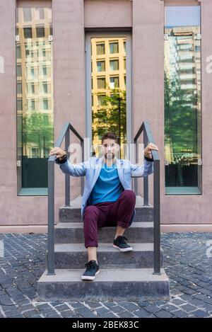 Porträt des glücklichen bärtigen jungen Mannes auf der Treppe sitzend Stockfoto