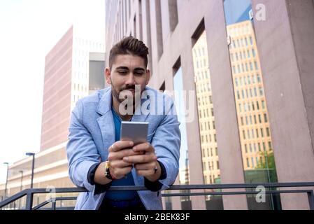Porträt eines schönen jungen Mannes lächelnd, wenn er sein Handy benutzt Stockfoto