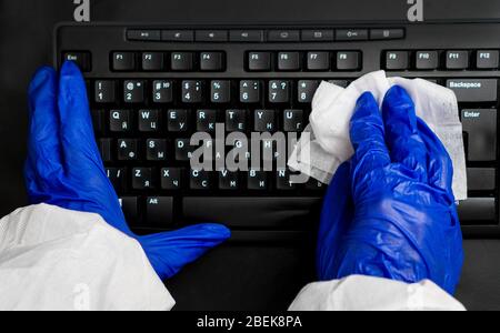 Hand in Schutzhandschuh mit Serviettenreinigungstastatur. Desinfektionskonzept Covid-19. Stockfoto