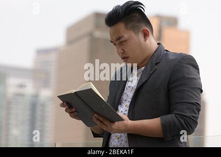 Junge übergewichtige asiatische Geschäftsmann Lesen Buch in der Stadt Stockfoto