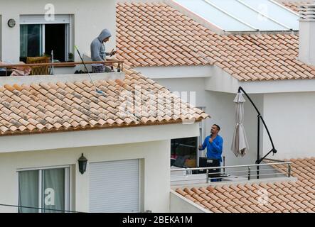 Altea La Vella, Provinz Alicante, Spanien, 21. März 2020, ein junger Mann auf seinem Balkon, der ein Handy benutzt, während sein Nachbar Musik auf seinem Computer macht Stockfoto