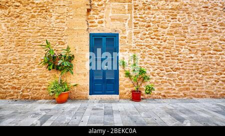 Alte Steinmauer mit blauer Tür und Topfblumen an einer Straße in Alcudia Altstadt, Mallorca, Spanien. Stockfoto