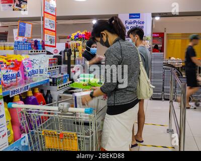 SINGAPUR – 9. April 2020 – Maskengetraene stellen sich an den geschäftigen Check-out-Schaltern des NTUC Fairprice Supermarkts in Singapur an Stockfoto