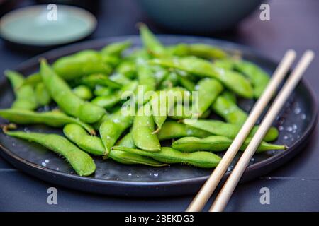 Gekochte grüne Edamame liegen auf einem dunklen Teller in einem japanischen Restaurant. Stockfoto