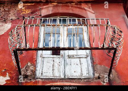 Abgerissene Balkon und Holztür eines verlassenen historischen Hauses außen mit rissigen und geschälten roten Wänden in Ulus, Ankara, Türkei. Stockfoto