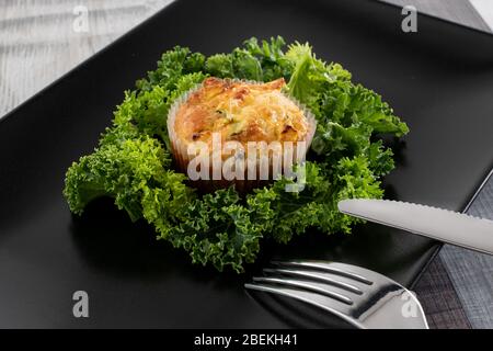 Frisch gebackene Zucchini- und Thunfisch-Muffins auf einem dunklen Teller mit Grünkohl. Vorschlag des Servierens des Gerichts. Stockfoto