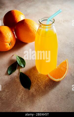 Frisch hausgemachter Orangensaft in einer Glasflasche mit Stroh und Orangen auf einem Tisch. Stockfoto
