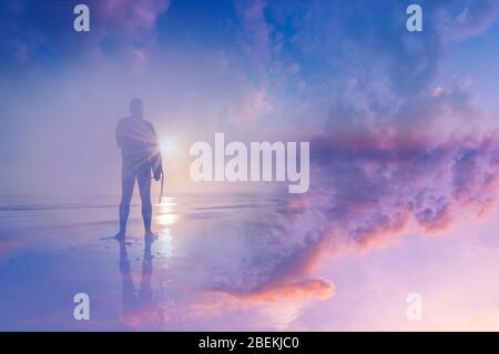 Silhouette eines Surfers am Strand mit Blick auf den Sonnenuntergang. Mit einer doppelten Belichtung des Himmels und einem abstrakten, experimentellen Traum wie Edit. Stockfoto