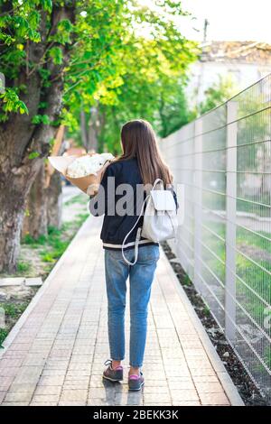 Mädchen mit einem Strauß von Kamillen. Mädchen mit einem Rucksack und einem Blumenstrauß. Stockfoto