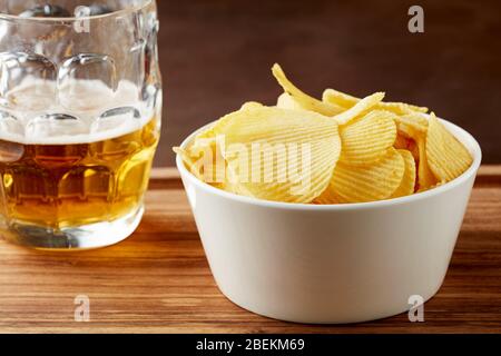 Kartoffelchips in einer weißen Schüssel und ein Glas Bier auf einem hölzernen Serviertablett Stockfoto