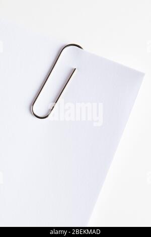 Büroklammer aus Metall, die an der Ecke eines weißen leeren Papiers befestigt ist. Nahaufnahme. Stockfoto
