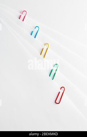 Bunte Büroklammern aus Kunststoff, die nacheinander an weißen leeren Papieren befestigt sind. Nahaufnahme. Stockfoto